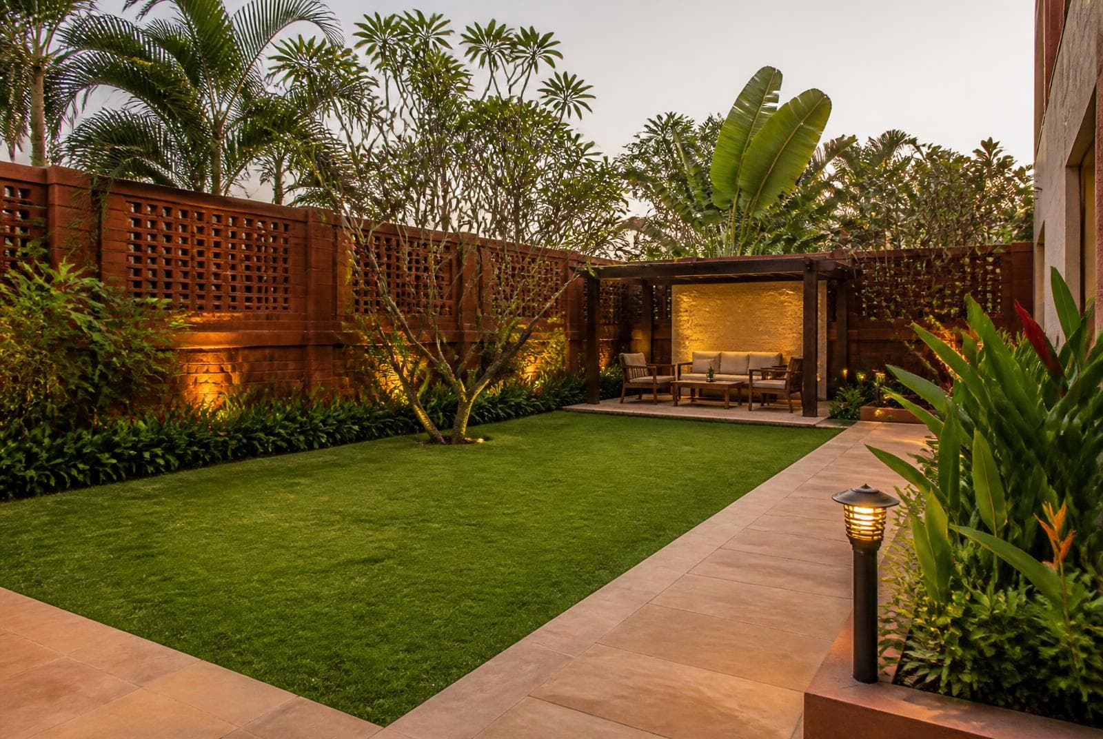 Landscaped hotel garden with lawn, shaded seating and evening lighting